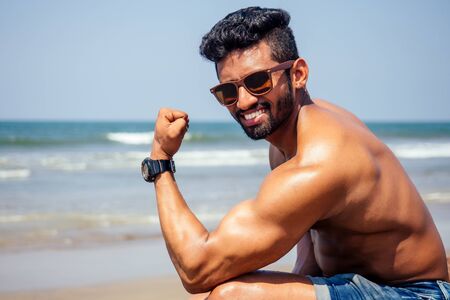 Topless athletic, muscular and healthy black man warm up instructor on the beach.indian male fashion model with denim shorts jeans and perfect body.healthy food and active beach vacationの写真素材