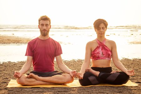 Young sportive couple girl and boy are practicing acroyoga exercises in the sunset on the beachの写真素材