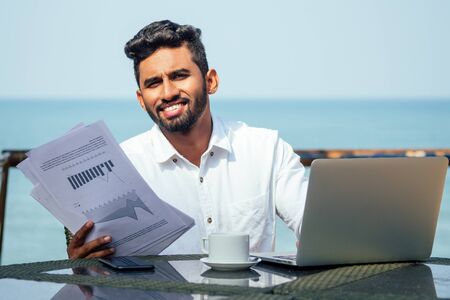 handsome and successful indian man in a stylish well-dressed freelancer working with a laptop on the...