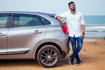 Successful young businessman sunglasses on a beach. Afro man leaning on his car parked in front of ocean on road trip enjoying peace and silence relaxing on nature.Summer vacations and travel conceptの写真素材