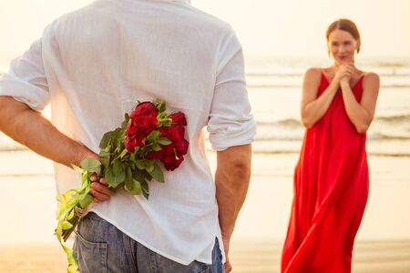 man giving roses to his surprise and wonder woman on the ocean beach. romantic date or wedding or valentines day concept by sea.loving couple celebrating March 8 Womens Day and happy birthdayの写真素材