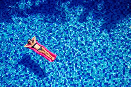 beautiful brunette girl floating on mattresses in the pool.fitness female model in black bikini...