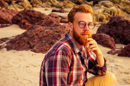 male freelancer bearded glasses hipster with a laptop remote work on the beach on the...