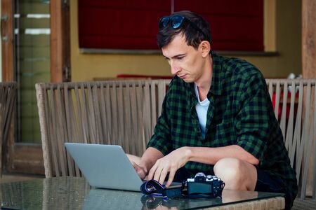 remote work surfing and freelance vacation. Young freelancer surfer businessman working laptop computer on the tropical beach in the summer cafe on the street veranda.man vacation in exotic country.の写真素材
