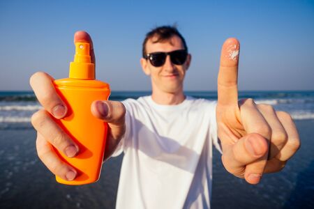 closeup of a young caucasian man wearing a white T-shirt applying sunscreen to his body against the sea ocean.の写真素材