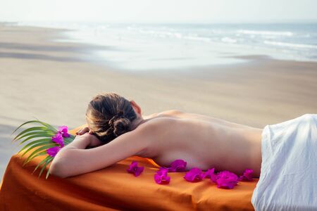 Ayurvedic relaxing massage ,health woman in spa salon getting massage the holiday beach.Beautiful girl enjoying day spa resort, lying down on the table treatment procedure.male master neck therapistの写真素材