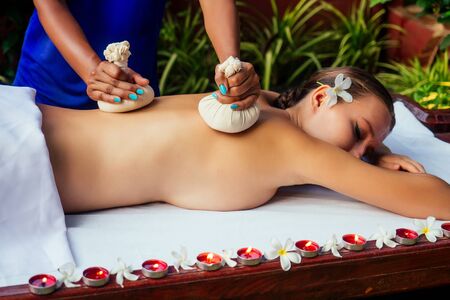 Portrait of young beautiful woman lying on a wooden table in spa environment flowers and candlesの写真素材