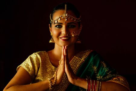 portrait indian beautiful female in golden rich jewelery and tradition saree professional make-up wearing bindi on head .Muslim Woman face portrait with bindis maang tikka ,nath,nose Pin welcomingの写真素材