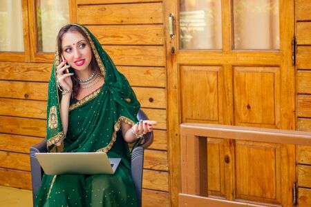 beautiful and young indian business woman in traditional india sari working with laptop veranda at...