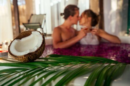 wedding night.beautiful bride and handsome groom relaxing in bath tropical flowers at luxury hotel resort.couple in love clink glasses eco bali spa.candles,romance date Valentines Day 14th Februaryの写真素材
