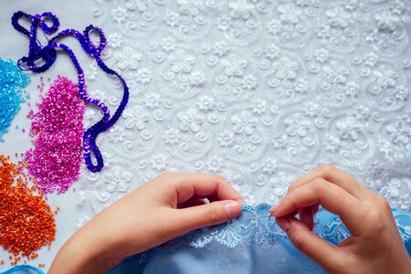 close-up hands of woman seamstress tailor dressmaker designer wedding dress sews beads to lace on a...