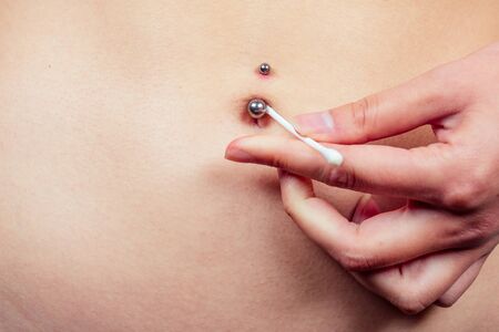 female navel piercing close-up with a cotton swab