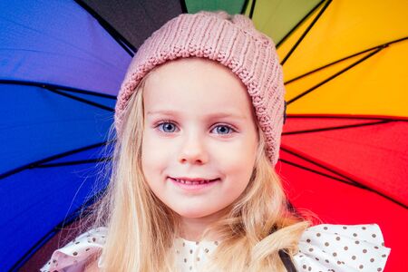 Happy funny beautiful blonde with blue eyes child with rainbow colorful umbrella in the autumn park....