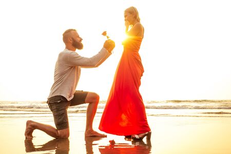 romantic February 14 Valentines Day summer holidays, relationship dating.love couple with bouquet flowers man in a white shirt and a blond woman in a long dress with a rose in his hand on the beachの写真素材