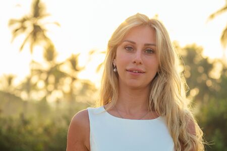 charming and beautiful bride in a beautiful white long wedding dress with long blond hair smiling at...