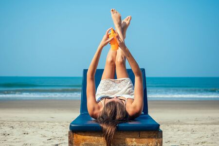 beautiful and sexy young woman is applying sunscreen on the body on the sea. Protection from ultraviolet rays and prevention against skin cancer on vacationの写真素材