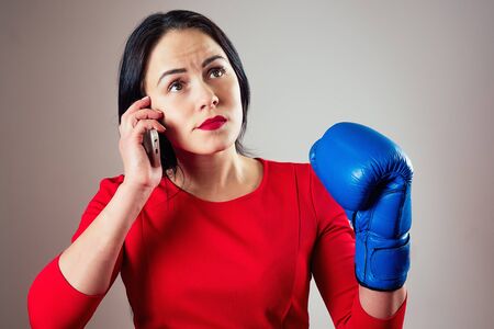 portrait of a beautiful brunette woman with boxing gloves and a phone in her arms in the gym. athlete with makeup red lipstick boxing. concept of female power, feminismの写真素材
