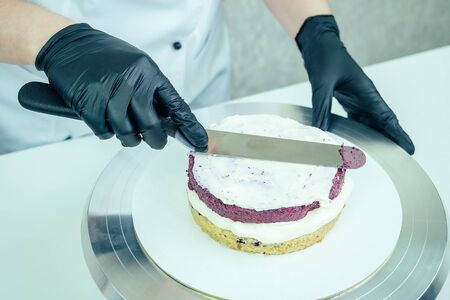 confectioner in black gloves and white work uniforms puts cream on the cake on the table. confectioner, cake, cooking.の写真素材