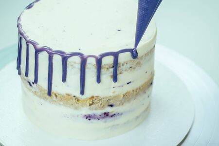 confectioner in black gloves and white work uniform adorns the cake in the kitchen. confectioner, cake, cooking. wedding and birthday cake with berriesの写真素材