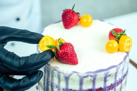confectioner in black gloves and white work uniform adorns the cake in the kitchen. confectioner,...