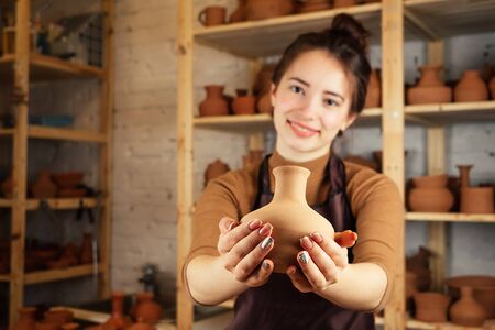 a young and cheerful woman holding a vase of clay. The potter works in a pottery workshop with clay. the concept of pottery mastery and creativityの写真素材