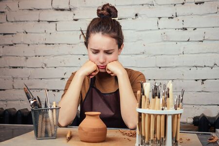 The concept of sadness and lack of ideas in creativity. A young and sad woman looks at a vase of...