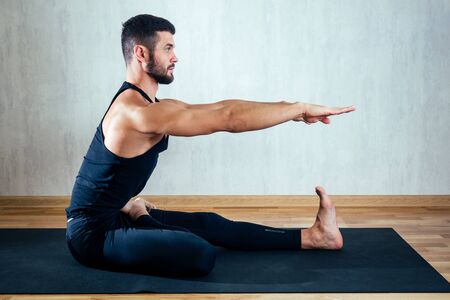 a man in dark sportswear practicing yoga on a dark background. asana on the floor on yoga mats. the...