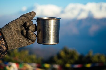 a metal cup with a hot drink in the hand against the background of the mountains. the concept of an active holiday in the mountains. tourizm in cold seasonの写真素材