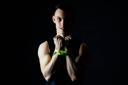 portrait young man measures his hand with a measuring tape in the gym on a dark backgroundの写真素材
