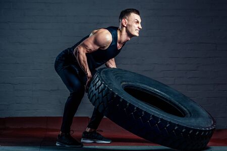 young man doing exercises with a tire in the gymの写真素材