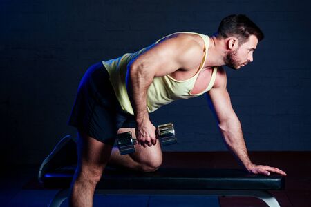 young handsome man in a yellow t-shirt is engaged with a dumbbell in the gymの写真素材