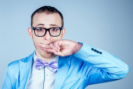 a man with glasses and a blue stylish suit covers his mouth with his hand. the concept of secrecy, confidentiality and privacyの写真素材