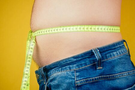 a fat man and a measuring tape on his belly stomach . concept of unhealthy nutritionの写真素材