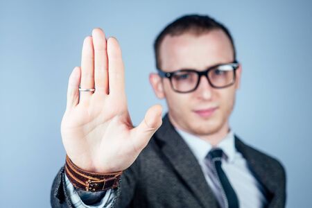 a man nerd freak with glasses and a gray stylish suit shows a stop gesture with his handsの写真素材