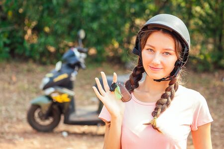 beautiful and young woman in a safety helmet sitting on a motorcycle bike and holds the keys. concept of safe driving a scooter and renting in Asiaの写真素材