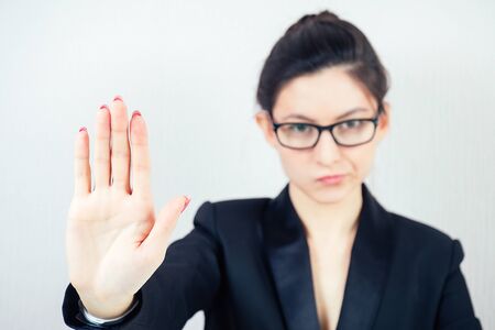 portrait of attractive strict brunette woman business lady in stylish business suit and glasses shows a hand gesture stop in the workplace officeの写真素材