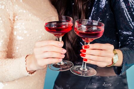 hands of two womens in evening cocktail shiny sequins dress are holding a glass of wine at a party...