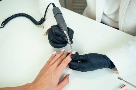 close-up hands of manicurist professional master of manicure woman in a black rubber gloves is apply a machine hardware manicure tool for removing cuticles of client in a beauty spa salon.の写真素材
