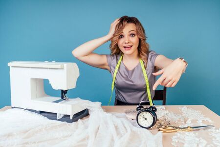 clock close-up on the table behind woman seamstress tailor dressmaker designer sews a wedding dress...