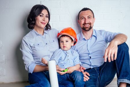 happy family handsome man in helmet hardhat and charming woman and their cute little son sitting on...