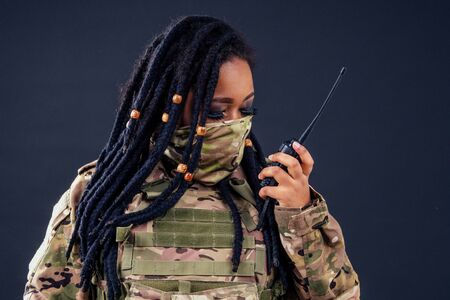 Woman in a military camouflage with a radio afro american army latin soldier in camouflage clothes hair dreadlocks evening makeup on a black background in the studio.の写真素材