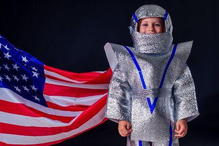 adorable female child in costume helmet playing bright foil silver cosmonaut in uniform with american flag black background in the studio.patriotism July 20, 1969 landing on the moon concept space dayの写真素材
