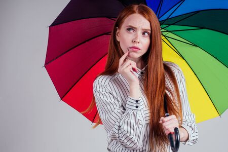 beautiful redhead girl on a white background in the style striped shirt with rainbow an umbrella....