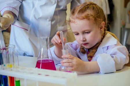 clever redhead school girl chemist in eyeglasses and white medical gown making science experiments...