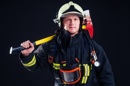 portrait strong fireman in fireproof uniform holding an ax in his hands black background studio