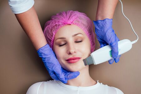 beauty female in medical gauze cap getting facial massage in spa salon.Ultrasonic scraber.hands in...
