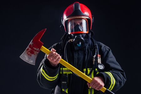 portrait strong fireman in fireproof uniform holding an ax in his hands black background studio.の写真素材