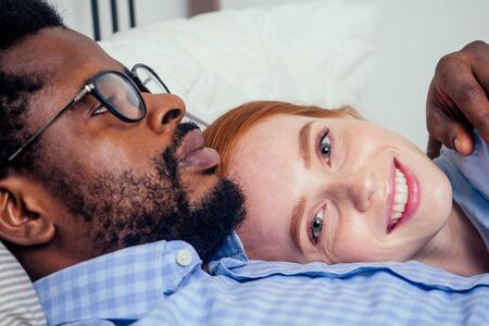 redhaired ginger caucasian happy female and multi-ethnic afro man together lying in bed...