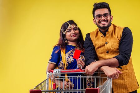 indian beautiful female carrying happy male in shopper metal truck in studio yellow background . black friday sales season conceptの写真素材