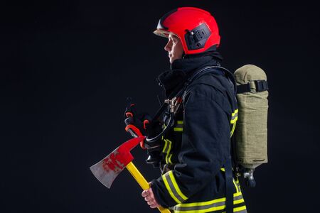 portrait strong fireman in fireproof uniform holding an ax in his hands black background studio.の写真素材